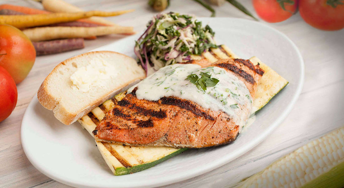 Fresh grill salmon with dill sauce over grilled zucchini and kale salad