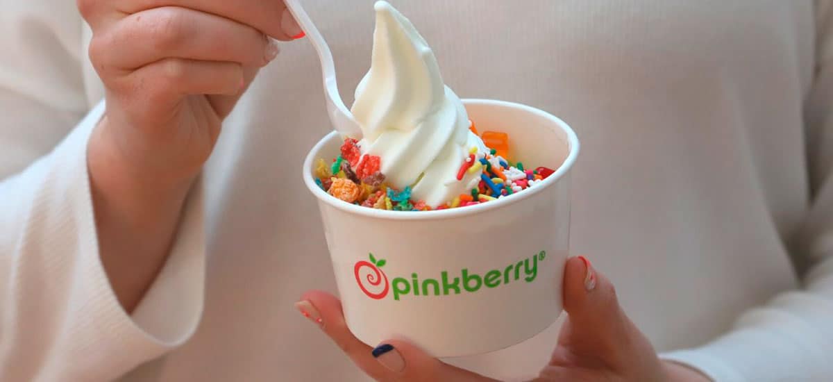 Woman holding a cup of pinkberry frozen yogurt topped with sprinkles and fruity pebbles.